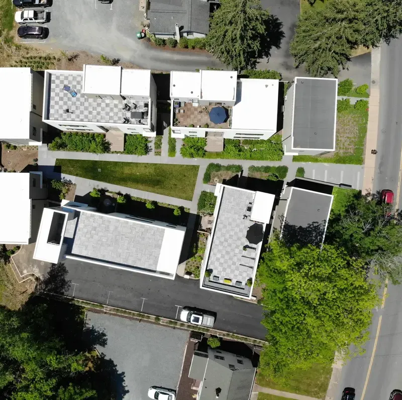 Aerial view of modern residential area featuring six white-roofed buildings surrounded by greenery and roads.