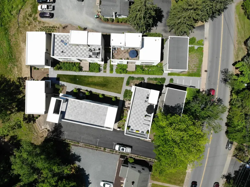 Aerial view of modern residential area featuring six white-roofed buildings surrounded by greenery and roads.