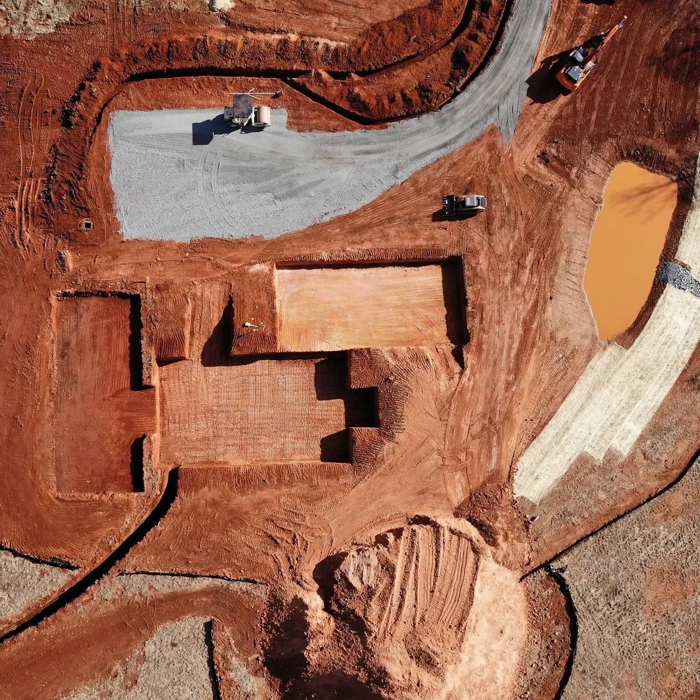 Aerial view of a construction site with red soil, featuring rectangular excavations.
