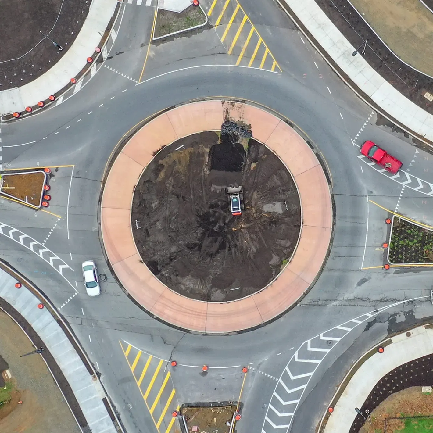 Aerial view of a roundabout under construction, featuring a central area with soil and a small red vehicle.