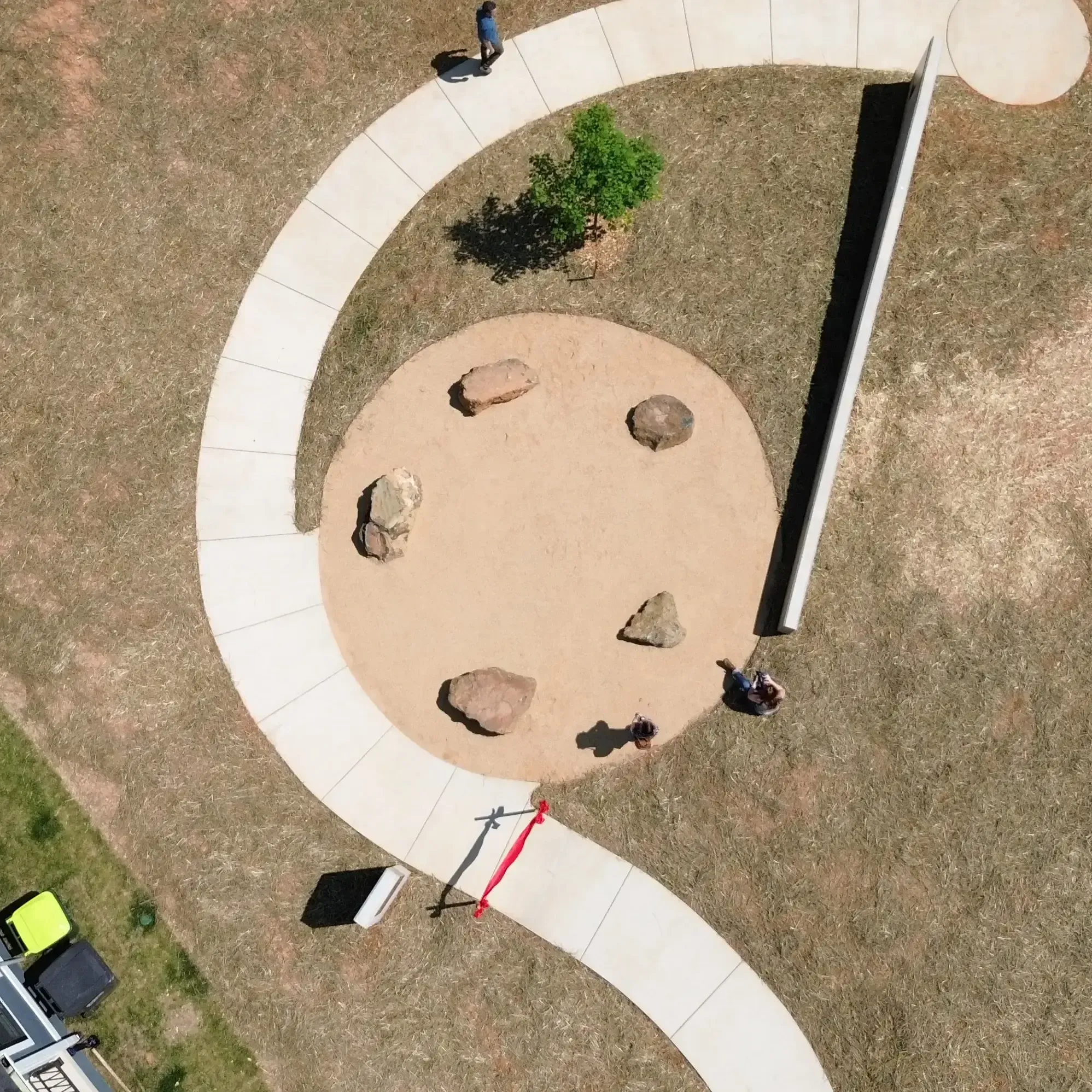 Aerial view of a curving concrete path surrounding a circular area with large rocks and a small tree.